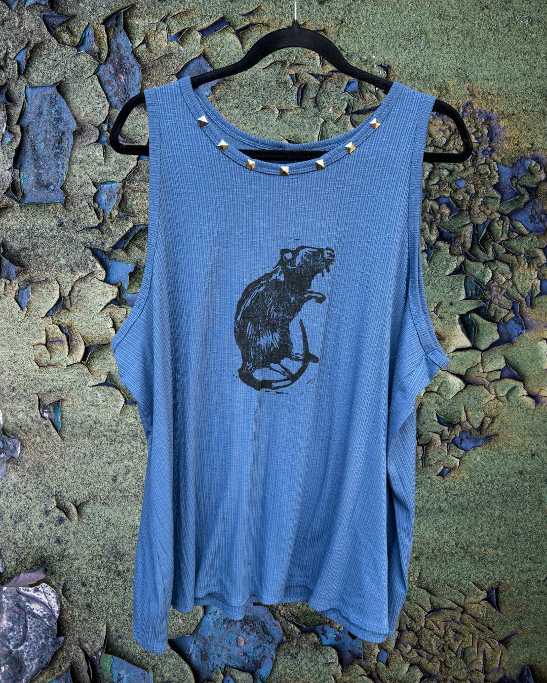 A sleeveless blue tank top with a ribbed texture featuring a row of silver pyramid studs around the neckline and a hand printed rat design on the front. 